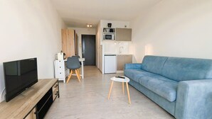 A modern living room with a flat-screen TV, a blue sofa, a small white table, and a wooden TV stand.