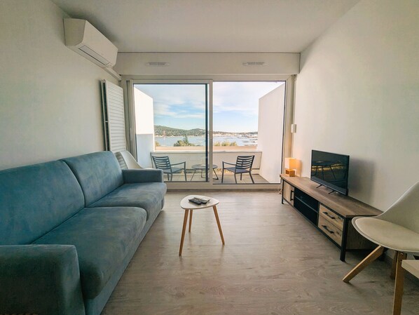 A modern living room with a sofa, a small table, a TV, and a balcony with a view.
