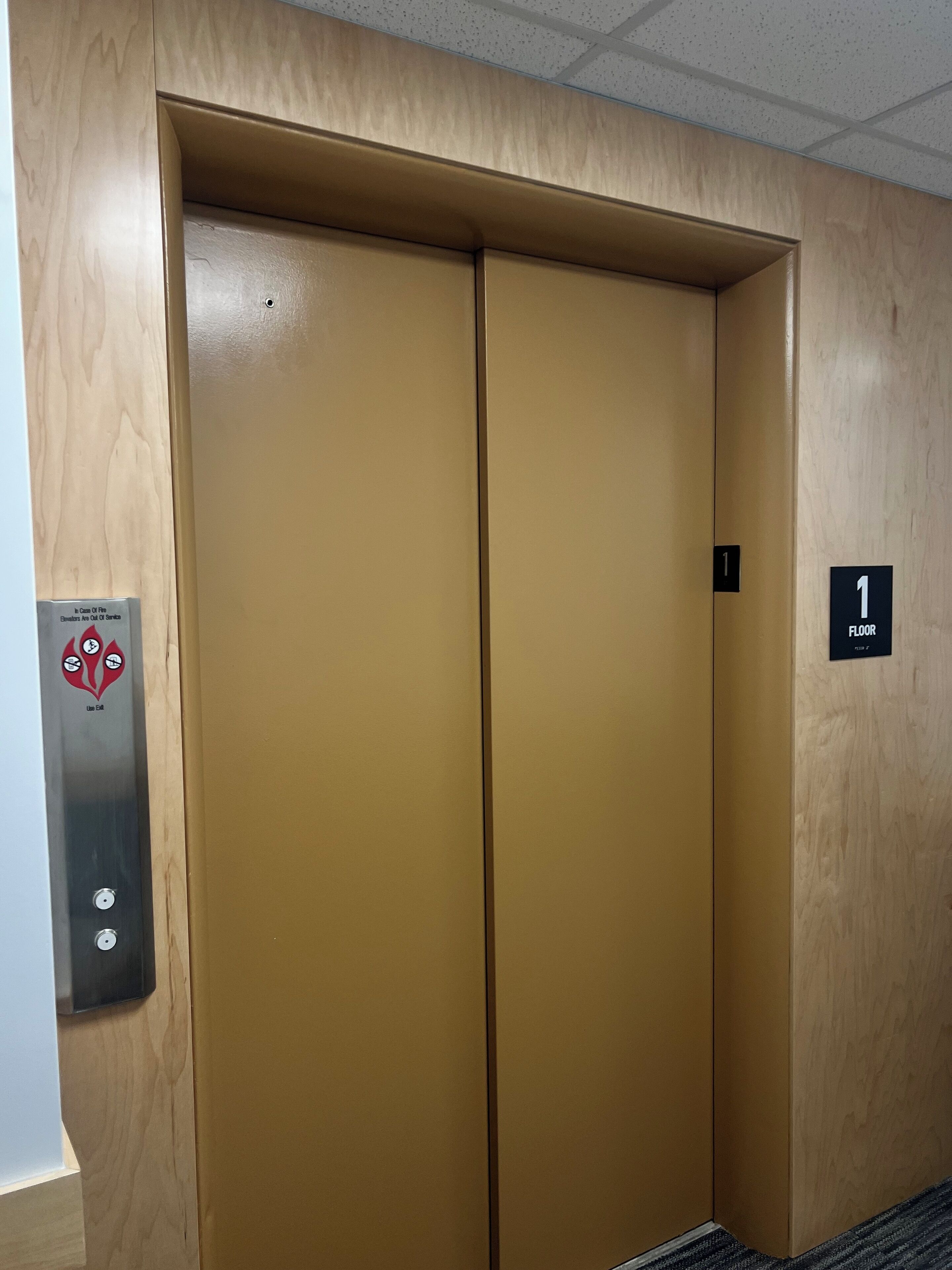 Ascensor cerrado con detalles de madera, un indicador de piso y un panel de alarma contra incendios.