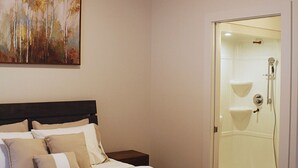 Una habitación de hotel con una cama, una mesita de noche, un cuadro y un área de ducha con mampara de vidrio.