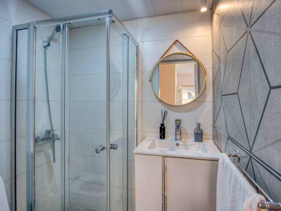 Un baño moderno con cabina de ducha de vidrio, un espejo redondo y un lavamanos blanco con un salpicadero de azulejos geométricos.