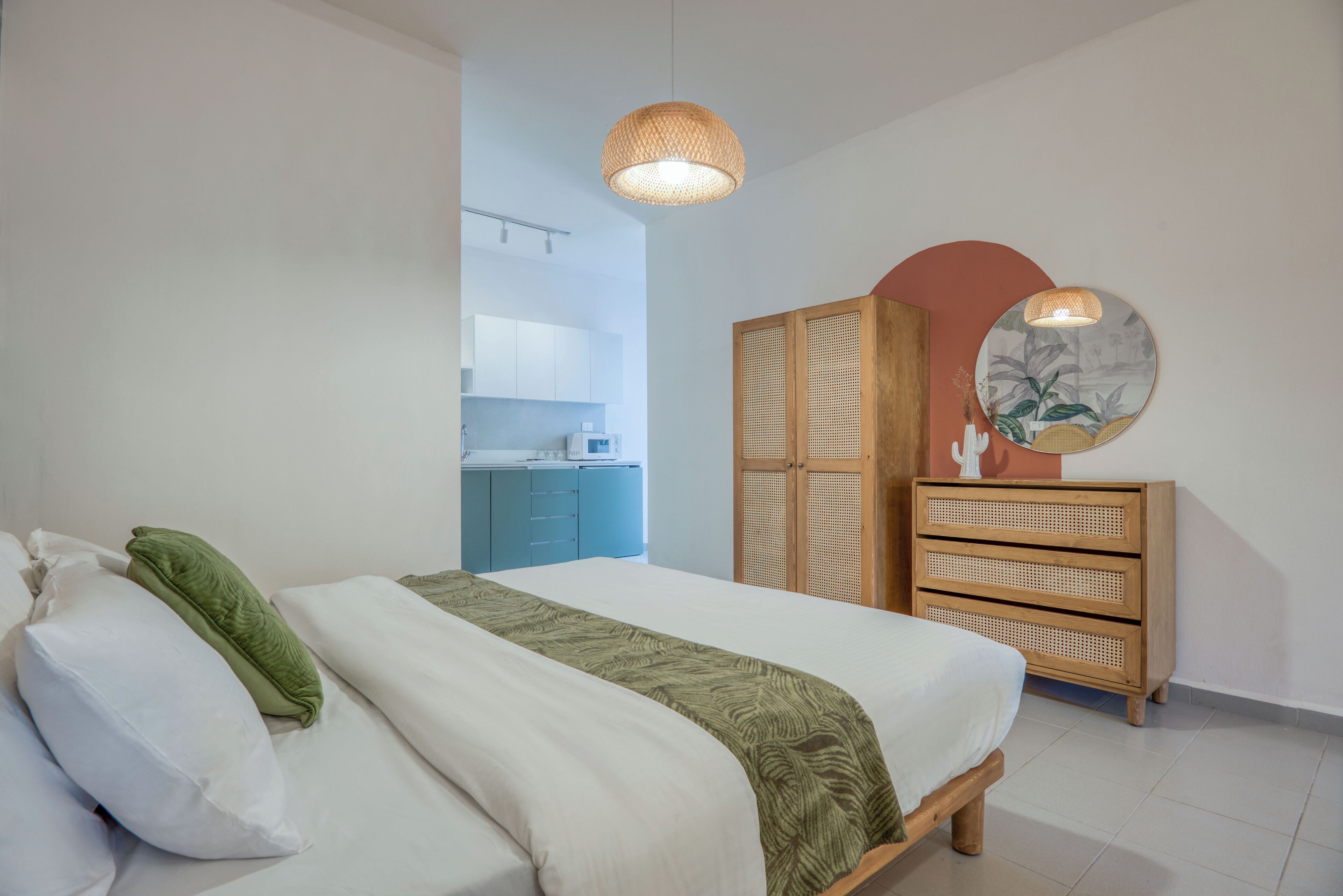 Een slaapkamer met een bed, een kledingkast, een spiegel en een kitchenette op de achtergrond.