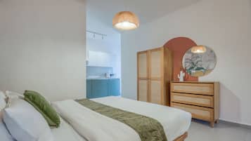 Een slaapkamer met een bed, een kledingkast, een spiegel en een kitchenette op de achtergrond.