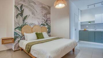 A bedroom with a bed, a woven headboard, a wall mural, and a kitchen area with cabinets and a sink.
