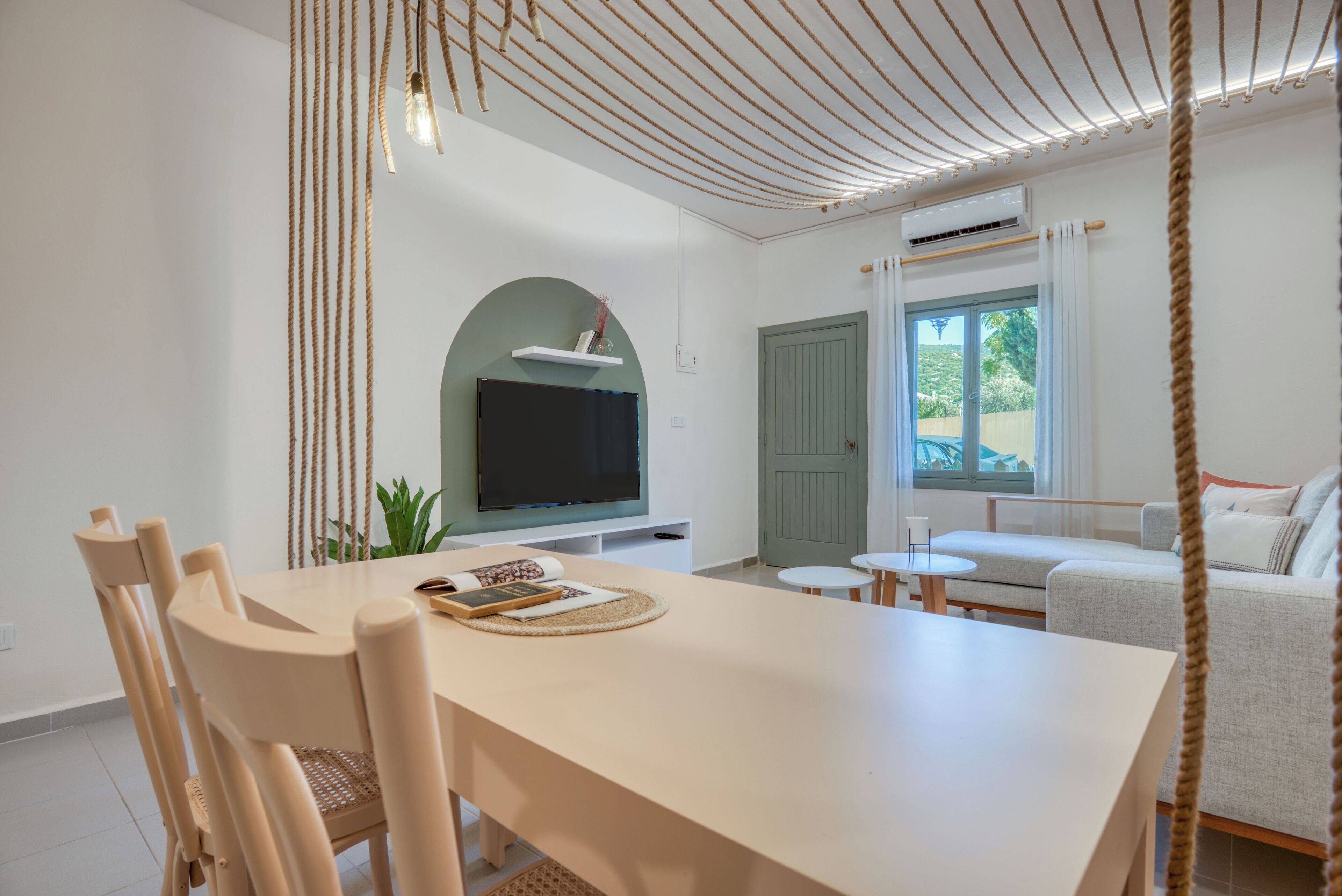 Una sala de estar moderna con comedor, un televisor de pantalla plana en la pared, una puerta verde y un ventanal grande.