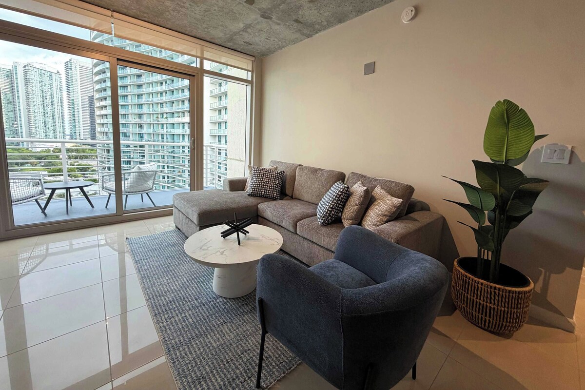 Una sala de estar moderna con sofá, sillón, mesa de centro y una planta en maceta.