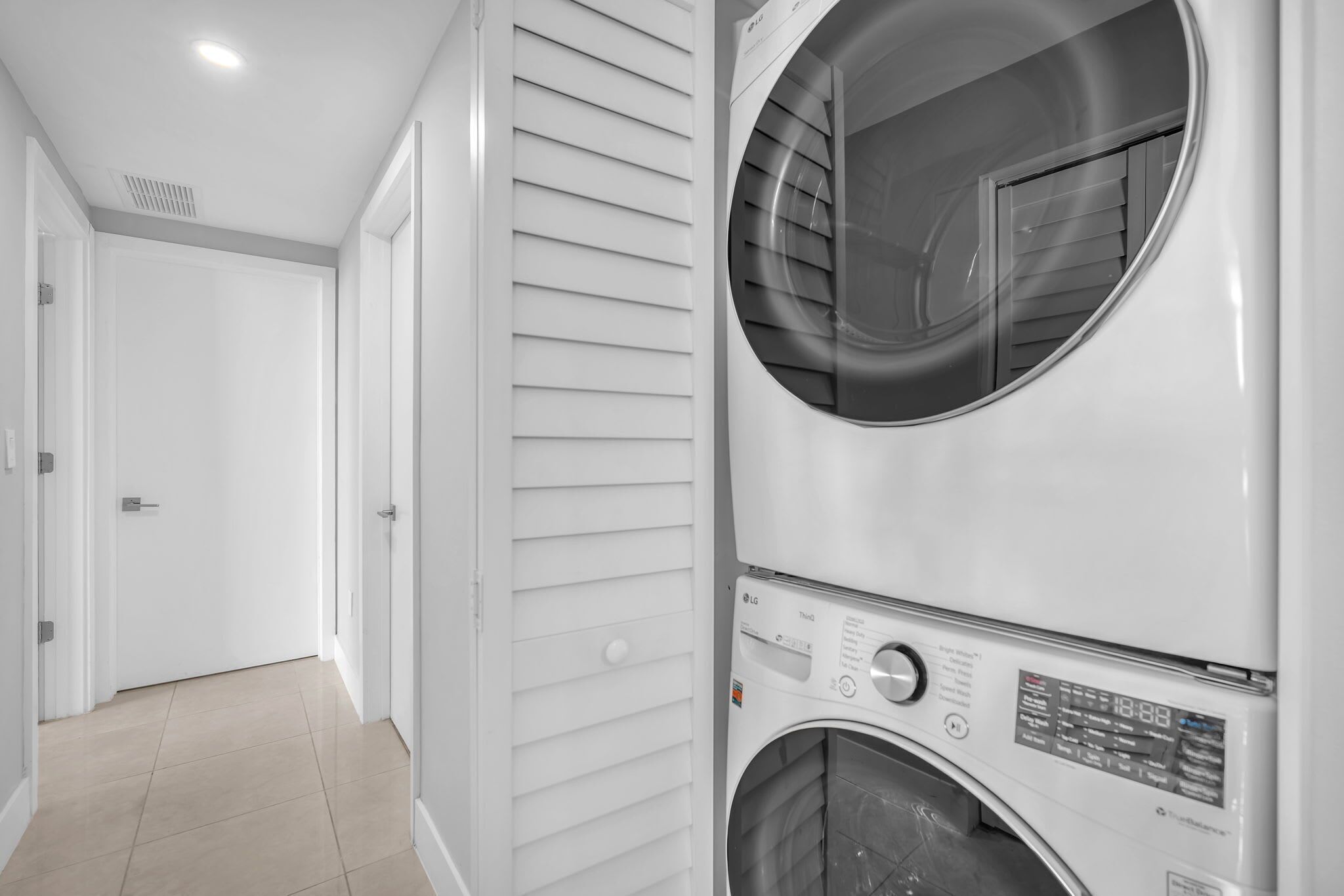 A laundry room with two stacked washers and dryers, a white door, and a tiled floor.