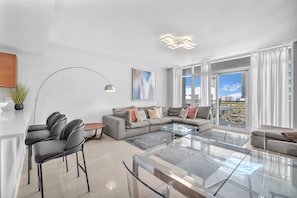 A modern living room with a glass coffee table, grey sofa, and a dining area with chairs. - Midtown Miami Condo with Free Parking (Miami)