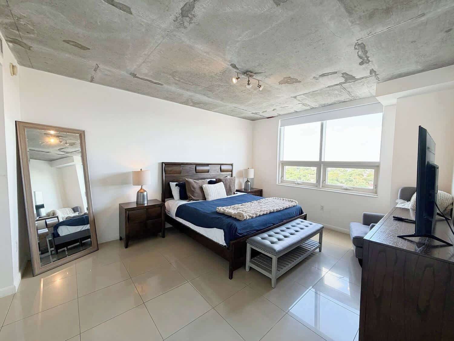 A bedroom with a bed, bedside tables, a mirror, a window, and a television.