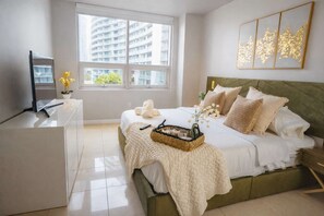 Quarto moderno com cama, mesa de cabeceira e janela com vista para edifícios.
