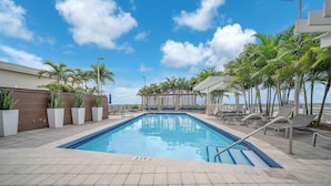 A swimming pool with a 3 FT depth marker, surrounded by lounge chairs and palm trees. - Midtown Miami Condo with Free Parking (Miami)