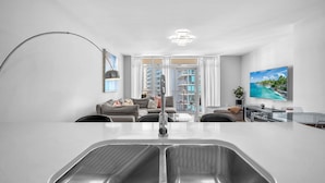 A modern kitchen with a large island, a dining area with a glass table, and a living room with a sofa and a TV. - Midtown Miami Condo with Free Parking (Miami)