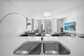 A modern kitchen with a large island, a dining area with a glass table, and a living room with a sofa and a TV. - Midtown Miami Condo with Free Parking (Miami)