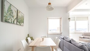 Ein modernes Wohnzimmer mit einem hellen Sofa, einem Esstisch mit Stühlen und einem großen Fenster mit Blick.