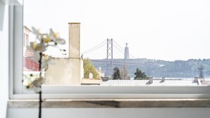 Blick auf eine Brücke durch ein Fenster, mit einem Gebäude und Bäumen im Vordergrund.
