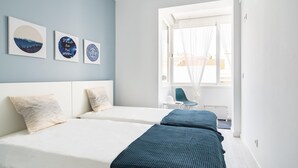Ein modernes Hotelzimmer mit zwei Betten, einem großen Fenster mit transparenten Vorhängen und drei an der Wand befestigten Kunstwerken.
