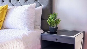 Een bed met een gestoffeerd hoofdbord, een nachtkastje met een plant, en een lade.
