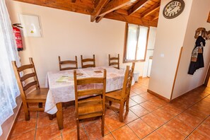 Un coin repas avec une table dressée pour quatre personnes, des chaises en bois, une horloge au mur et un extincteur.