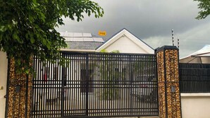 A gated property with a paved driveway, a white building with a tiled roof, and a logo on the gate.