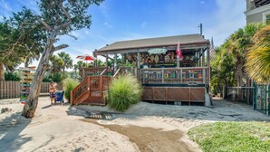 Un bar frente al mar con terraza de madera, asientos al aire libre y un letrero.