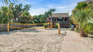 Una cancha de voleibol de playa con red, palmeras y un edificio con un cartel al fondo.