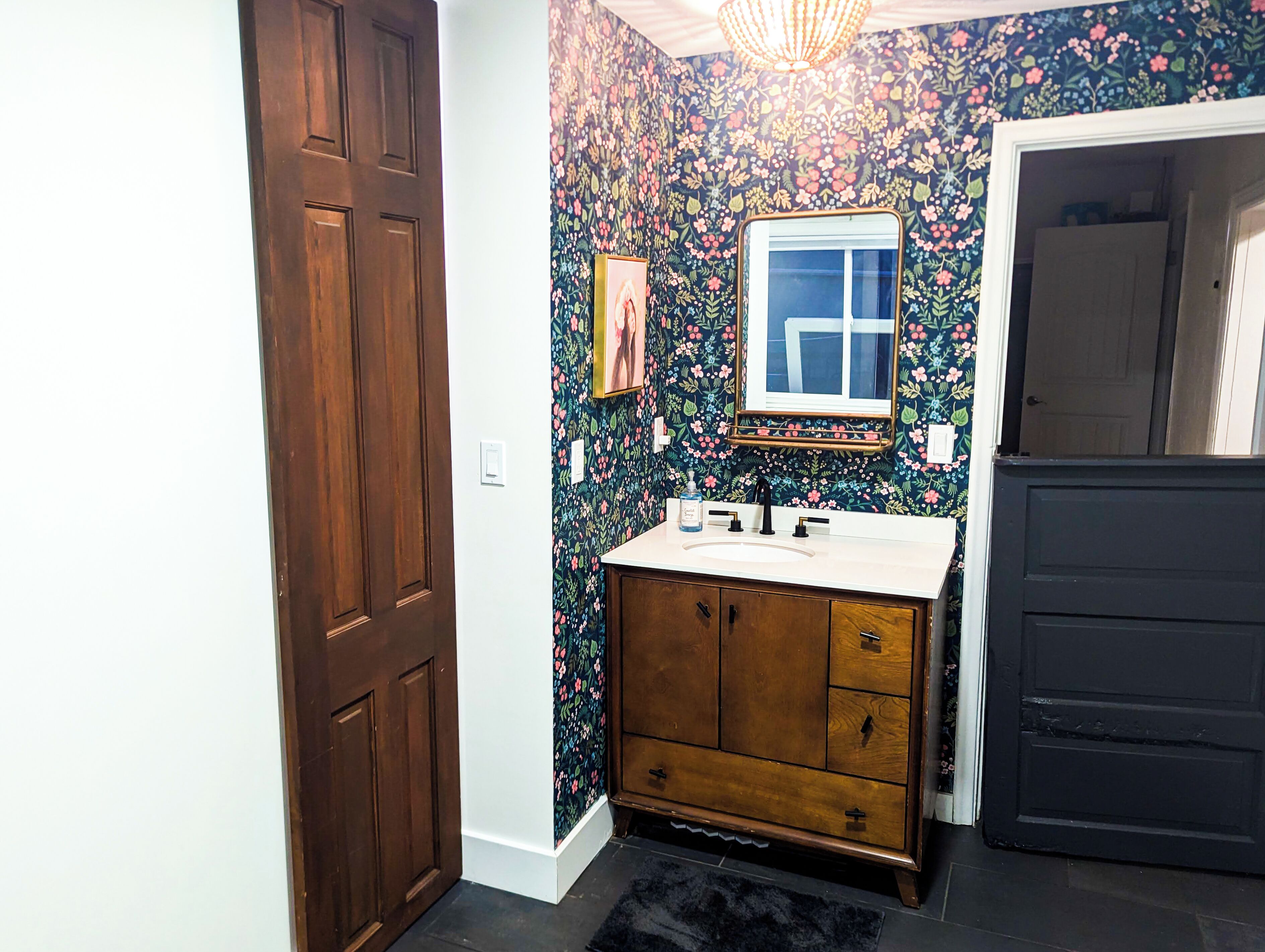 A bathroom with a wooden vanity, a mirror, and a floral wallpaper.