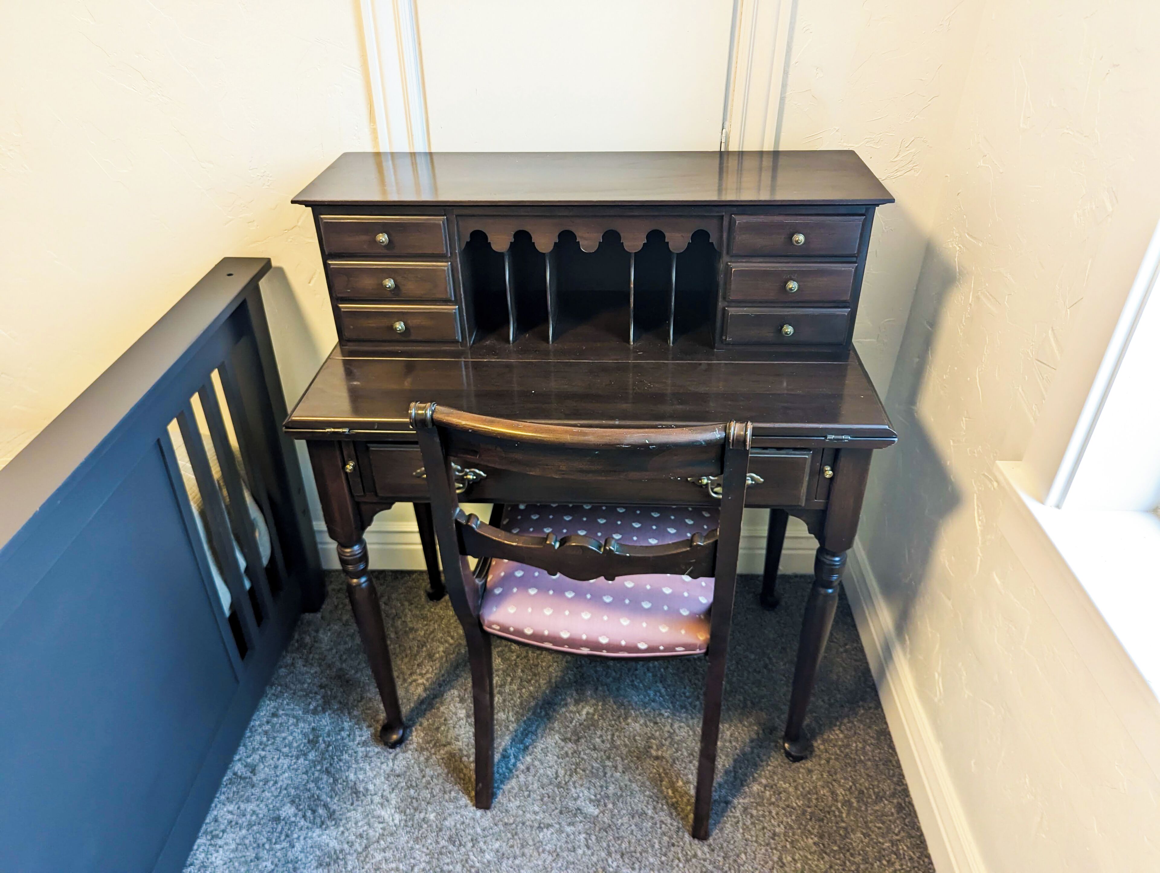 A dark wooden desk with multiple drawers and a chair with a polka dot cushion.