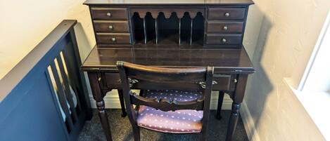 A dark wooden desk with multiple drawers and a chair with a polka dot cushion.