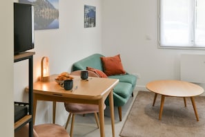 Une pièce avec une table en bois, un canapé vert, une petite table ronde, une lampe et un téléviseur.