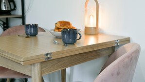 Un tavolo di legno con due tazze, un cucchiaio e una ciotola di croissant. Una candela accesa è sul tavolo.