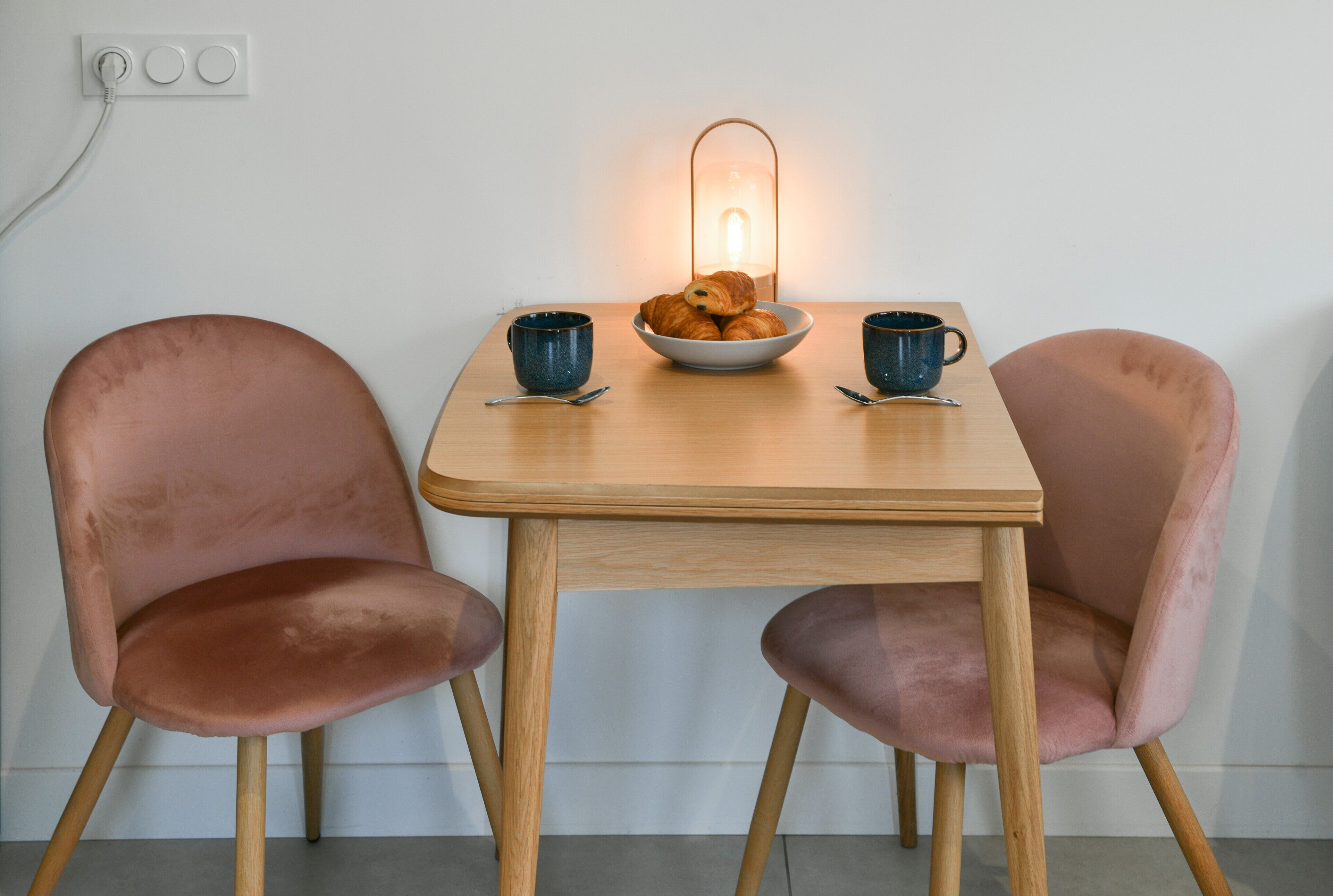 Een tafel met een schaal croissants, twee blauwe kopjes en een tafellamp.