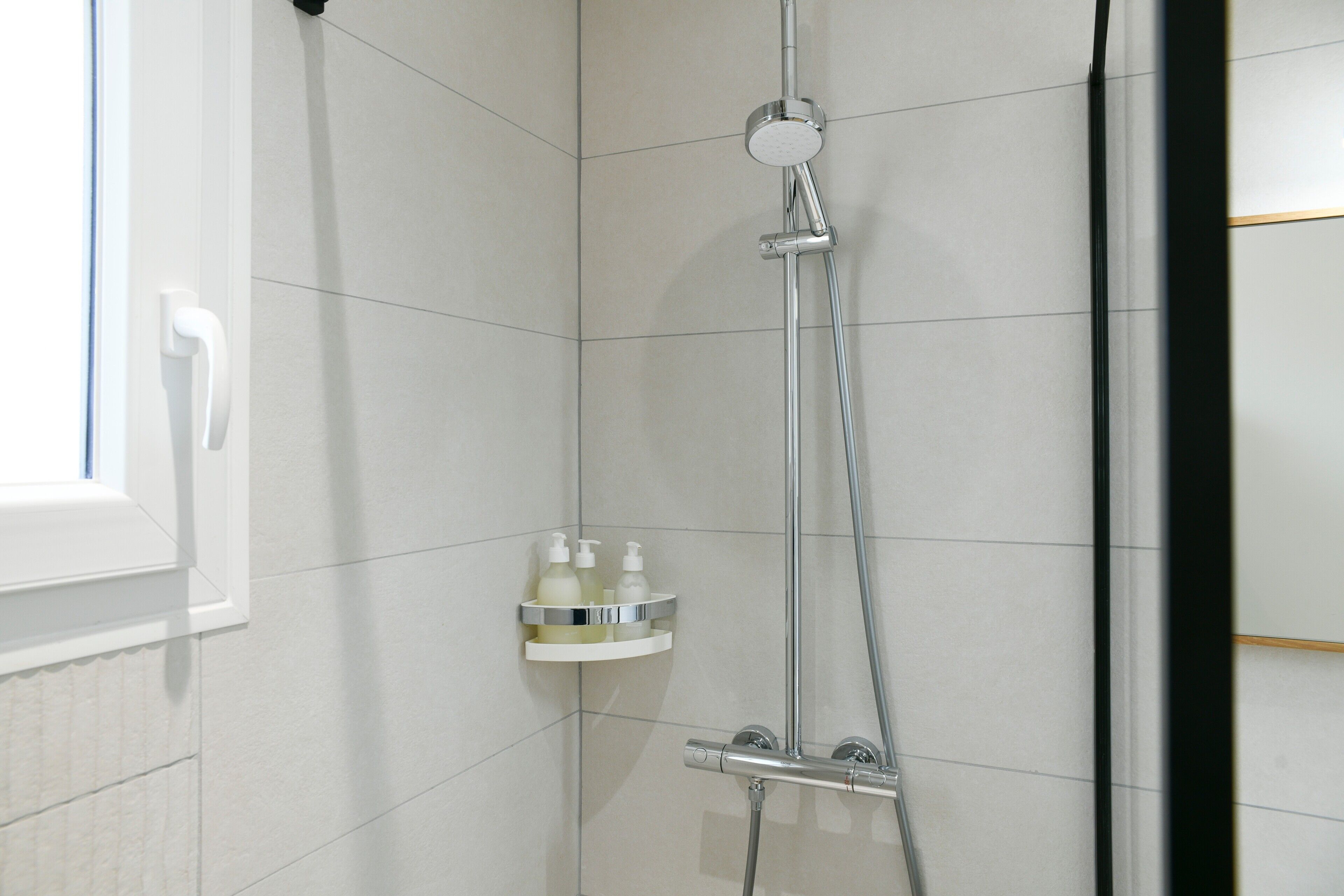 Une douche équipée d’un pommeau de douche à main, d’un robinet mural et d’une étagère pour les articles de toilette.