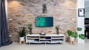 A living room with a stone wall, a flat-screen TV, a white entertainment unit, and potted plants.