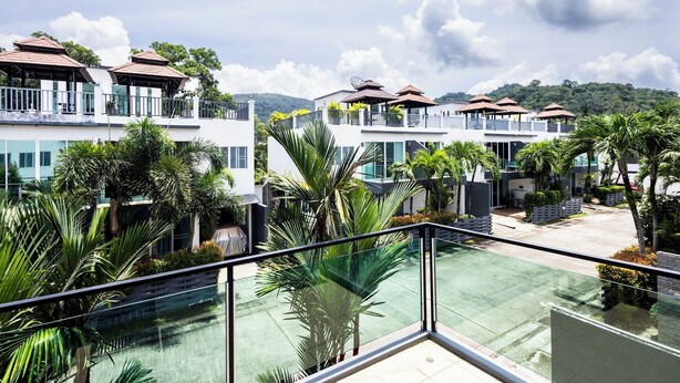 A modern hotel with multiple balconies, lush greenery, and a clear view of the surrounding landscape.