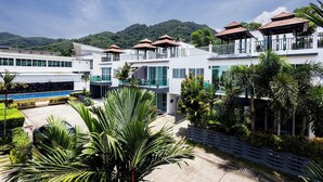 A modern hotel with multiple balconies, a swimming pool, and lush greenery.
