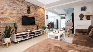 A modern living room with a brick wall, flat-screen TV, white entertainment unit, brown sofa, and a ceiling fan.