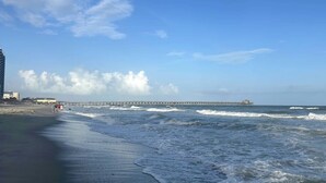 A beach with waves, a pier, and buildings in the background. - 2 BR Retreat by the waterfront in 
Little River, SC (Little River)