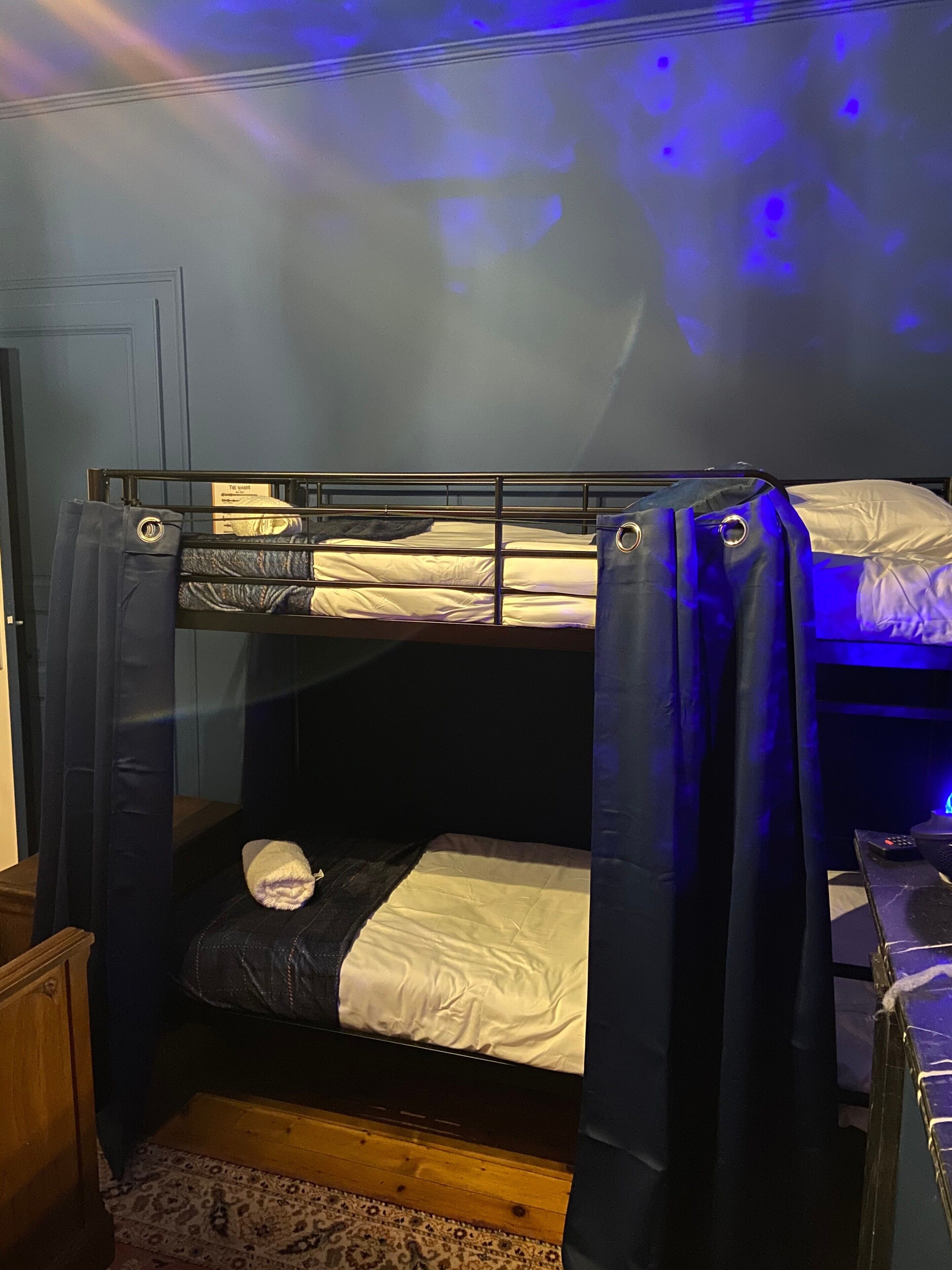 A bunk bed with a curtain, a wooden floor, and a small table with a remote control.