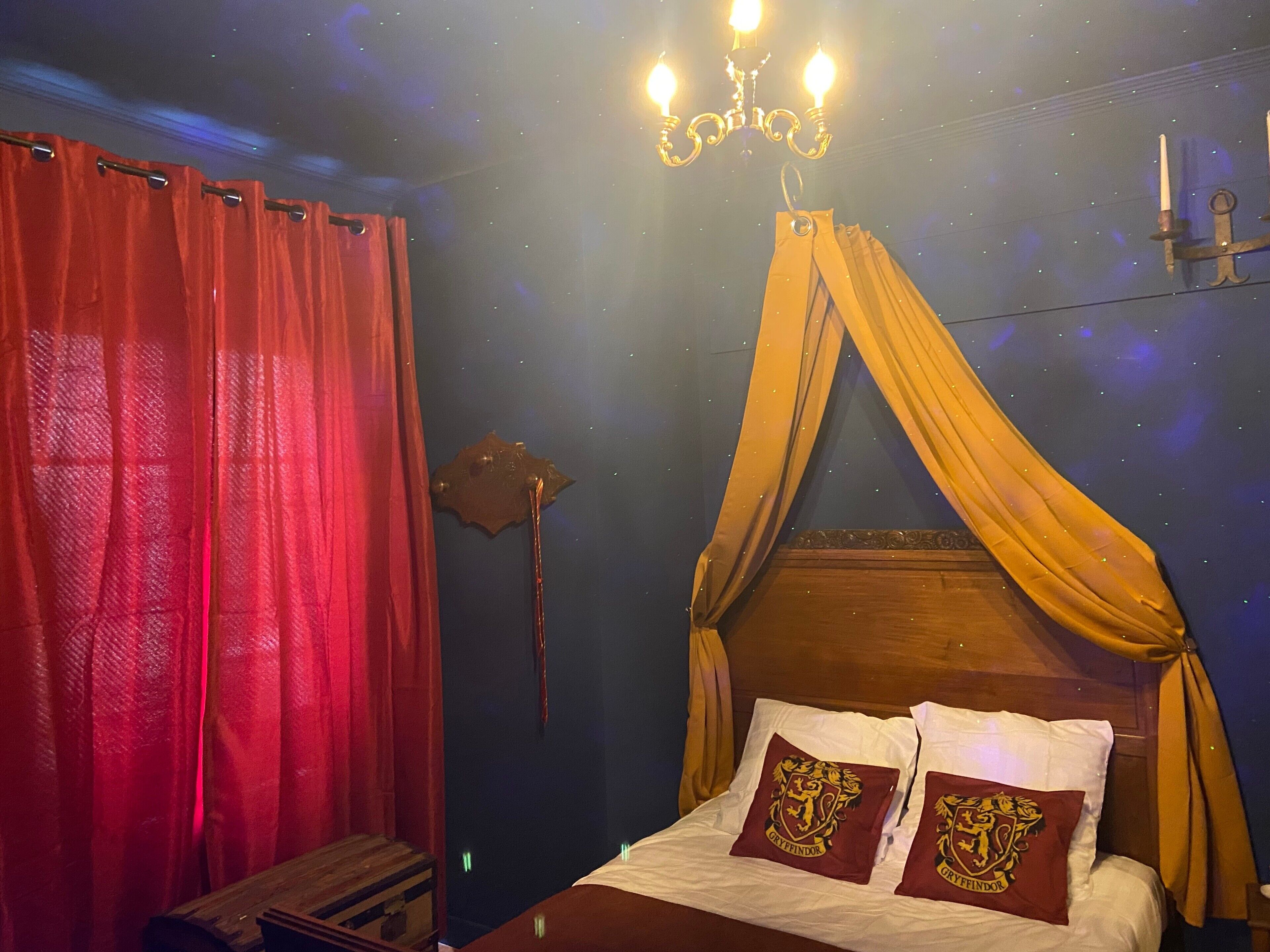 Una camera da letto con una testiera in legno, tende rosse, un soffitto stellato e un lampadario.