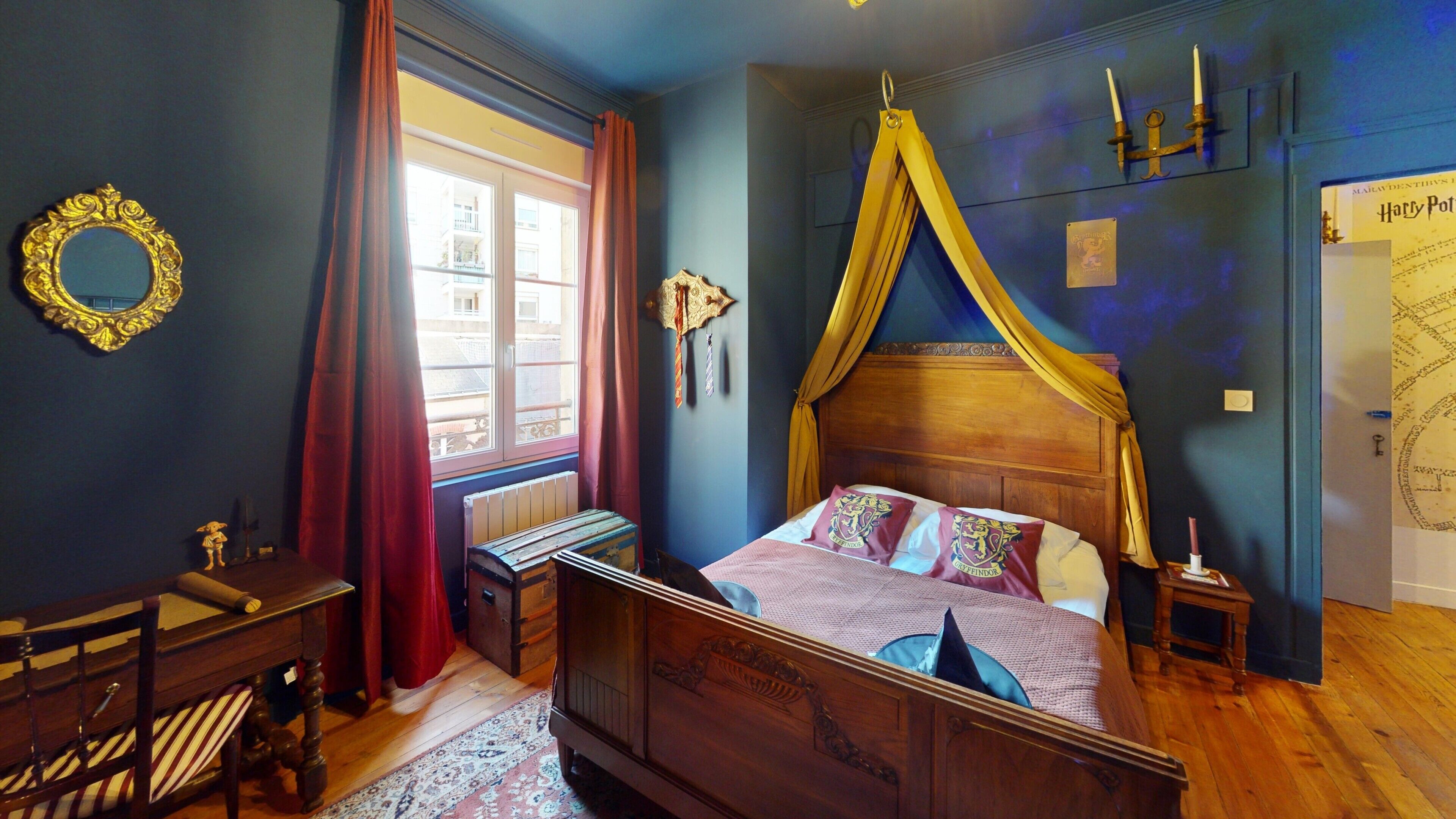 Un dormitorio con una cama con dosel, un escritorio de madera, una silla, una mesita de noche y un espejo en la pared.