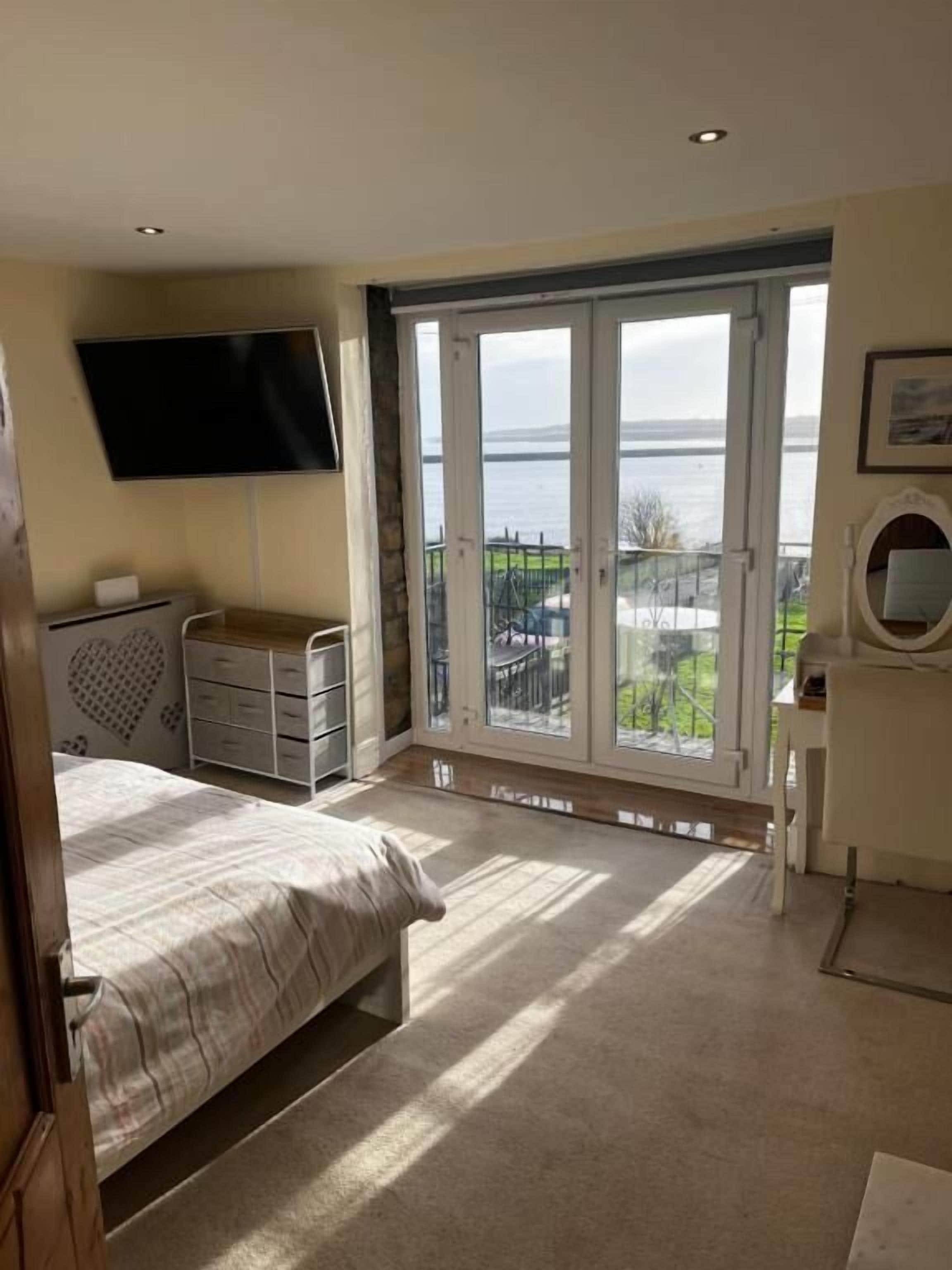 A bedroom with a bed, a dresser, a TV, and a balcony with a view of the sea.