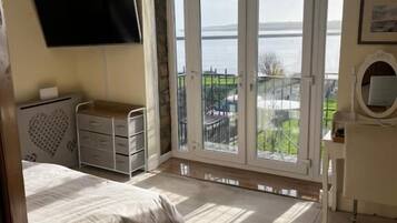 A bedroom with a bed, a dresser, a TV, and a balcony with a view of the sea.