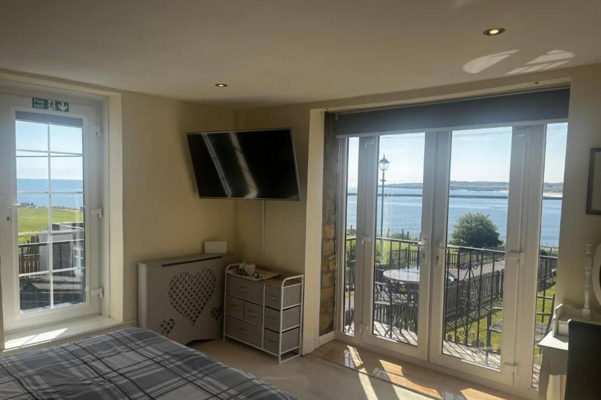 A bedroom with a bed, a dresser, a TV, and a balcony with a view of the sea.