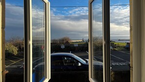 Udsigt gennem åbne døre til en parkeringsplads med en bil, en klar himmel og et fjerntliggende vandområde.