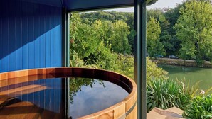 Ein Whirlpool mit Holzkante, Blick auf einen See und einen bewaldeten Hügel.