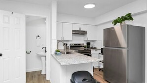 A modern kitchen with white cabinetry, a stainless steel refrigerator, and a granite countertop. - Stay West Side | 2 BR | Minutes from Downtown (West Columbia)