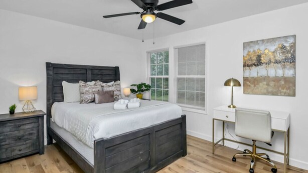 A modern bedroom with a dark wood bed, bedside lamps, a desk with a chair, and a ceiling fan. - Stay West Side | 2 BR | Minutes from Downtown (West Columbia)