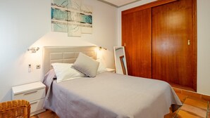 Un dormitorio con cama, mesita de noche, decoración en la pared y un armario de madera.