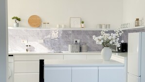 Une cuisine moderne avec des meubles blancs, un plan de travail en marbre, un four encastré et un coin repas comprenant une table et des chaises.
