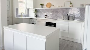 Une cuisine moderne avec des meubles blancs, un four encastré, un lave-vaisselle et un grand îlot central.